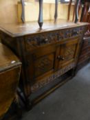 A REPRODUCTION CARVED OAK SMALL SIDE CABINET WITH ONE LONG FRIEZE DRAWER OVER A TWO DOOR CUPBOARD,