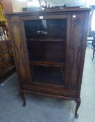 A CARVED OAK  SINGLE GLAZED DOOR DISPLAY CABINET, WITH SINGLE DRAWER BELOW, RAISED ON CABRIOLE
