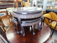 A SOUTH EAST ASIAN CARVED WOODEN CIRCULAR GLASS TOP LOW TABLE AND FOUR QUADRANT TABLES UNDER