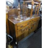 A 1920's/30's OAK SIDEBOARD, TWO DRAWERS OVER TWO CUPBOARDS, HAVING A LOW BACK WITH CENTRAL CIRCULAR