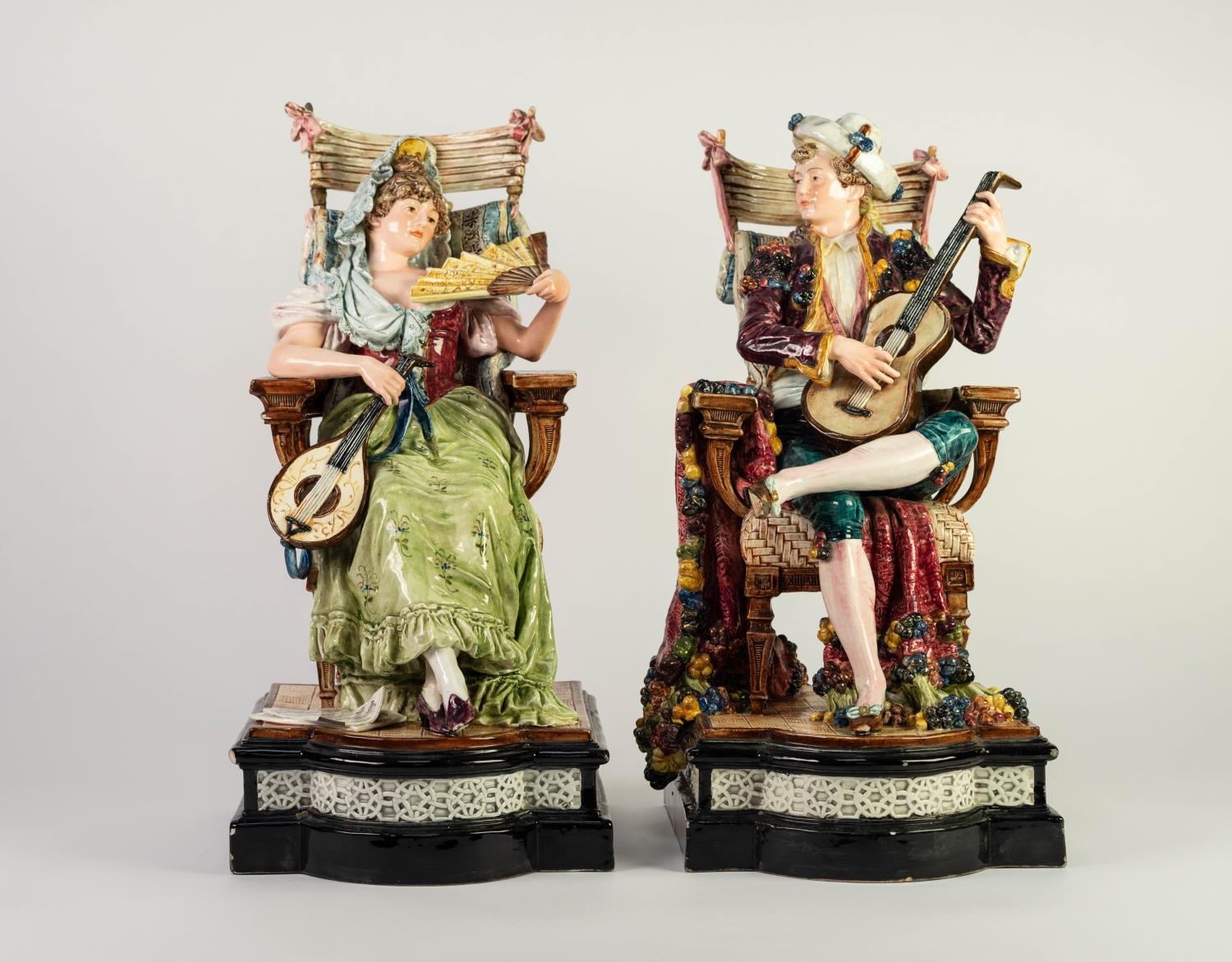 PAIR OF LATE NINETEENTH CENTURY CONTINENTAL FAIENCE FIGURE SEATED IN CHAIRS, he with guitar and