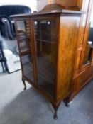 AN EARLY TWENTIETH CENTURY OAK TWO GLASS PANELLED DOOR DISPLAY CABINET ON CABRIOLE SUPPORTS