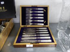 A WALNUT CASE CONTAINING SIX PAIRS OF ENGRAVED ELECTROPLATE FISH EATERS WITH MOTHER OF PEARL HANDLES