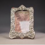 EMBOSSED SILVER FRONTED DESK TOP PHOTOGRAPH FRAME, of shaped oblong form, decorated with masks and