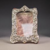 EMBOSSED SILVER FRONTED DESK TOP PHOTOGRAPH FRAME, of shaped oblong form, decorated with masks and