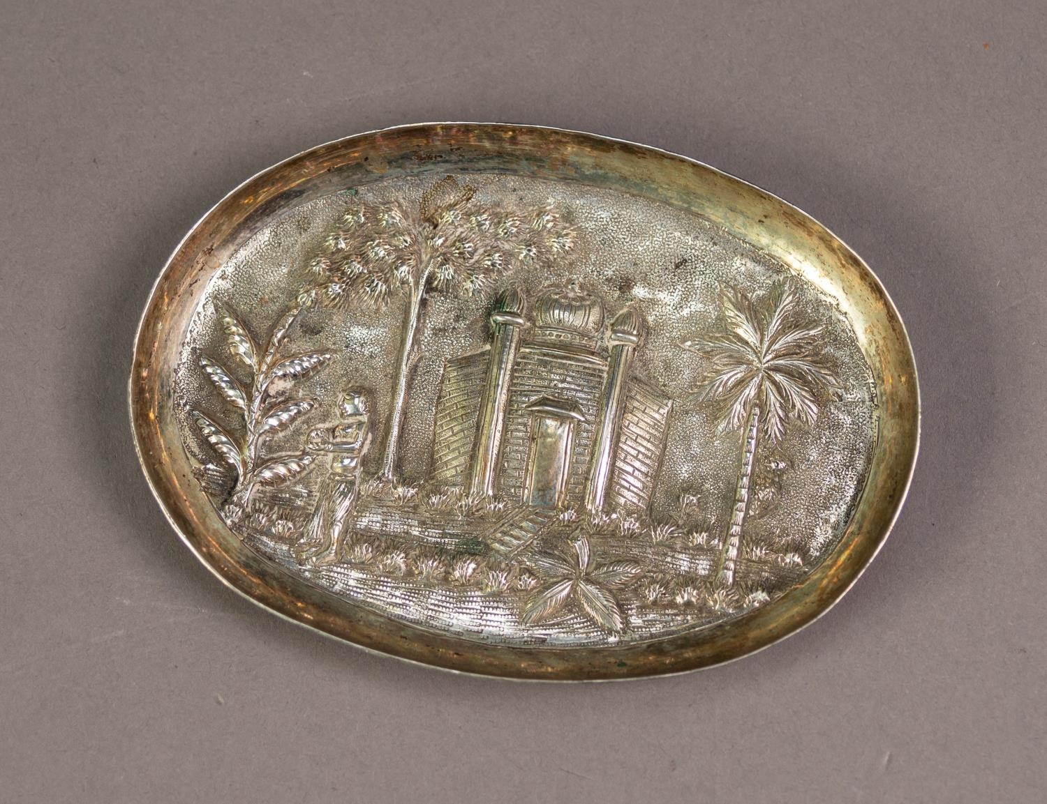 ASIAN EMBOSSED SILVER COLOURED METAL OVAL, SHALLOW DISH, decorated with a temple, figure and palm