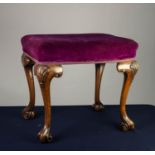 EARLY TWENTIETH CENTURY CARVED WALNUT STOOL, the oblong top covered in purple plush, and raised on