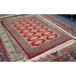 PAKISTAN BOKHARA RUG, with two rows of primary guls on a crimson field divided by three rows of