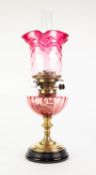 VICTORIA BRASS AND CRANBERRY GLASS OIL TABLE LAMP, of typical form with glass reservoir, fading