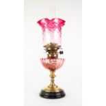 VICTORIA BRASS AND CRANBERRY GLASS OIL TABLE LAMP, of typical form with glass reservoir, fading