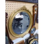 A LATE VICTORIAN/EDWARDIAN OVAL BEVELLED WALL MIRROR IN GILT GESSO FRAME WITH FLORIATED CRESTING AND