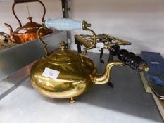 AN ANTIQUE BRASS TRIVET WITH TURNED WOOD HANDLE AND A BRASS KETTLE WITH BLUE GLASS HANDLE