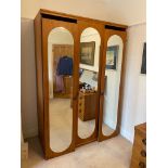 A TEAK WARDROBE, ENCLOSED BY THREE DOORS EACH WITH AN ARCH TOPPED MIRROR, ON PLINTH BASE, 4?7? WIDE,