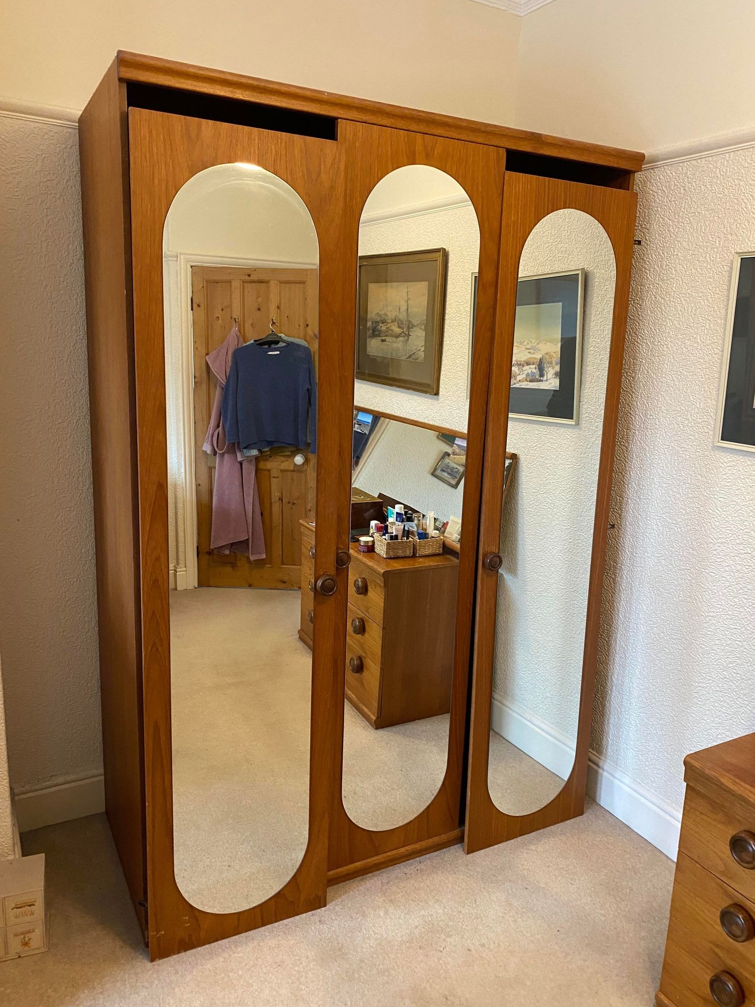 A TEAK WARDROBE, ENCLOSED BY THREE DOORS EACH WITH AN ARCH TOPPED MIRROR, ON PLINTH BASE, 4?7? WIDE,