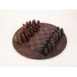 A TWENTIETH CENTURY AFRICAN CIRCULAR CARVED AND CHEQUERED WOODEN CHESS BOARD with dark and lighter