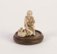 JAPANESE MEIJI PERIOD CARVED SECTIONAL IVORY OKIMONO OF A STREET VENDOR, modelled seated, holding