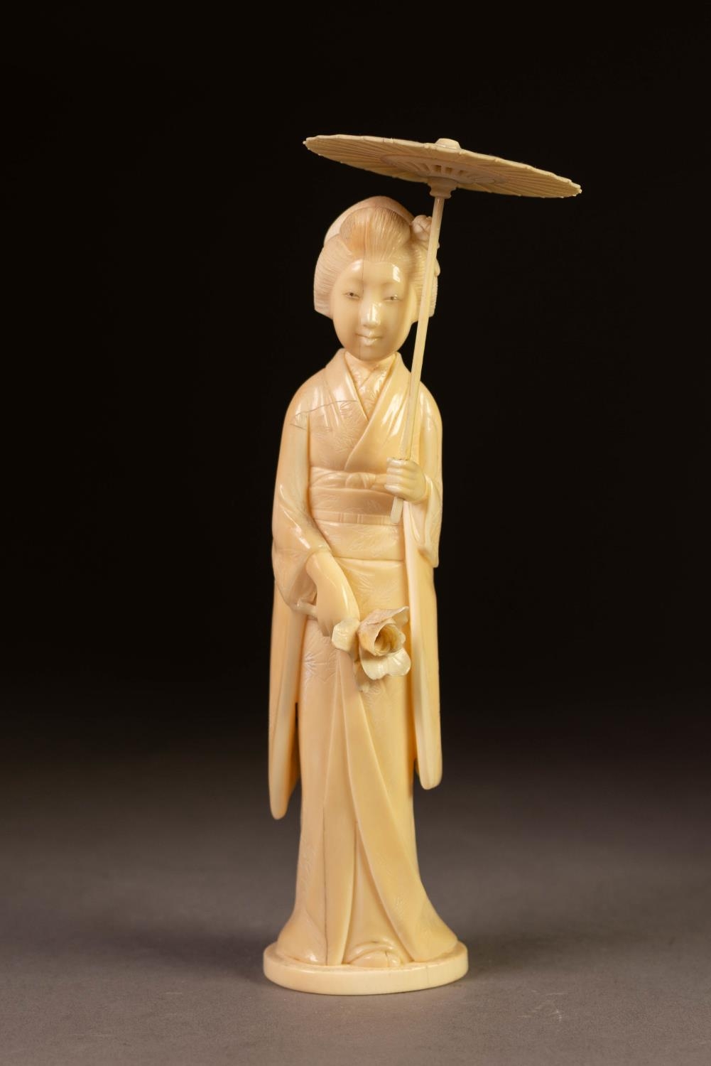 JAPANESE MEIJI PERIOD CARVED IVORY OKIMONO OF A GEISHA, modelled carrying a rose and open parasol,
