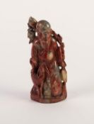 CHINESE CARVED MOTTLED RED SOAPSTONE FIGURE OF A SAGE, modelled standing with a young deer at his