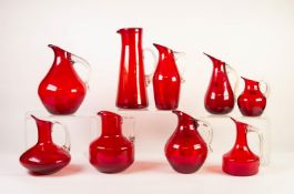 COLLECTION OF NINE WHITEFRIARS RED GLASS JUGS WITH CLEAR GLASS HANDLES, various shapes, 10 ¾? (27.