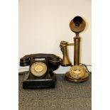 A black Bakelite telephone and a reproduction brass stick telephone.