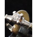 An 18ct white gold solitaire ring set with a brilliant cut diamond and tapered baguette cut
