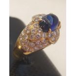 An 18ct yellow gold ring set with a cabochon cut sapphire and diamond set shoulders, (K).