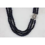 A triple row blue /black cultured pearl necklace on a stone set white metal clasp, L. 44cm, together