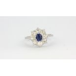 An 18ct white gold (stamped 750) cluster ring set with a sapphire surrounded by old cut diamonds,