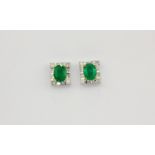 A pair of 18ct white gold (stamped 750) earrings set with oval cut emeralds surrounded by