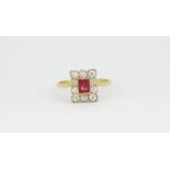 A yellow metal (tested 18ct gold) cluster ring set with a baguette cut ruby and brilliant cut