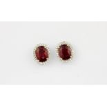 A pair of 18ct white gold (stamped 750) cluster earrings set with an oval cut ruby surrounded by