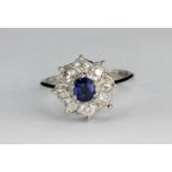 An 18ct white gold (stamped 750) cluster ring set with a sapphire surrounded by old cut diamonds,