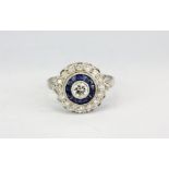 A white metal (tested 18ct gold) ring set with a brilliant cut diamond surrounded by sapphires and