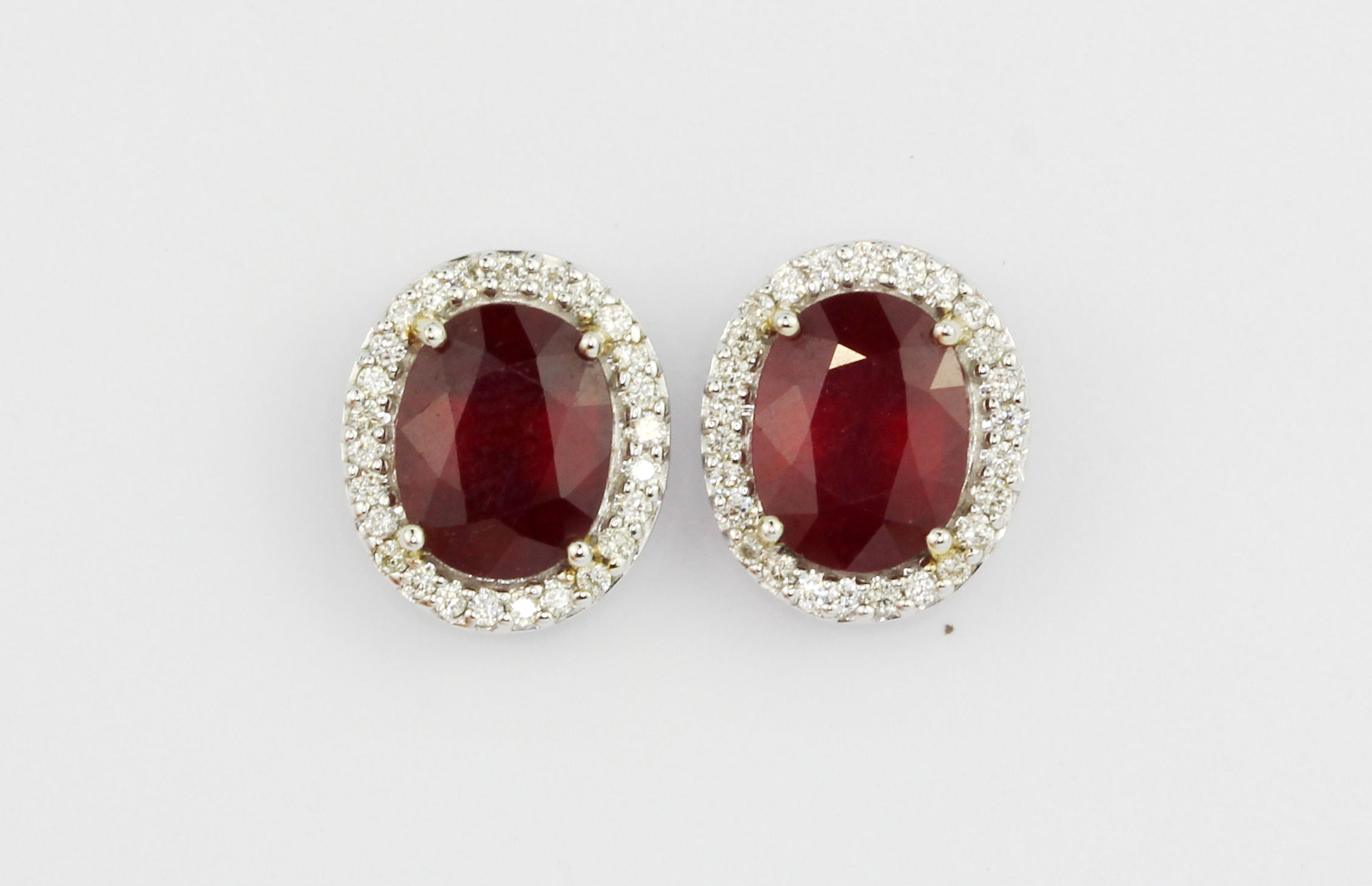 A pair of 18ct white gold (stamped 750) cluster earrings set with an oval cut ruby surrounded by