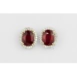 A pair of 18ct white gold (stamped 750) cluster earrings set with an oval cut ruby surrounded by