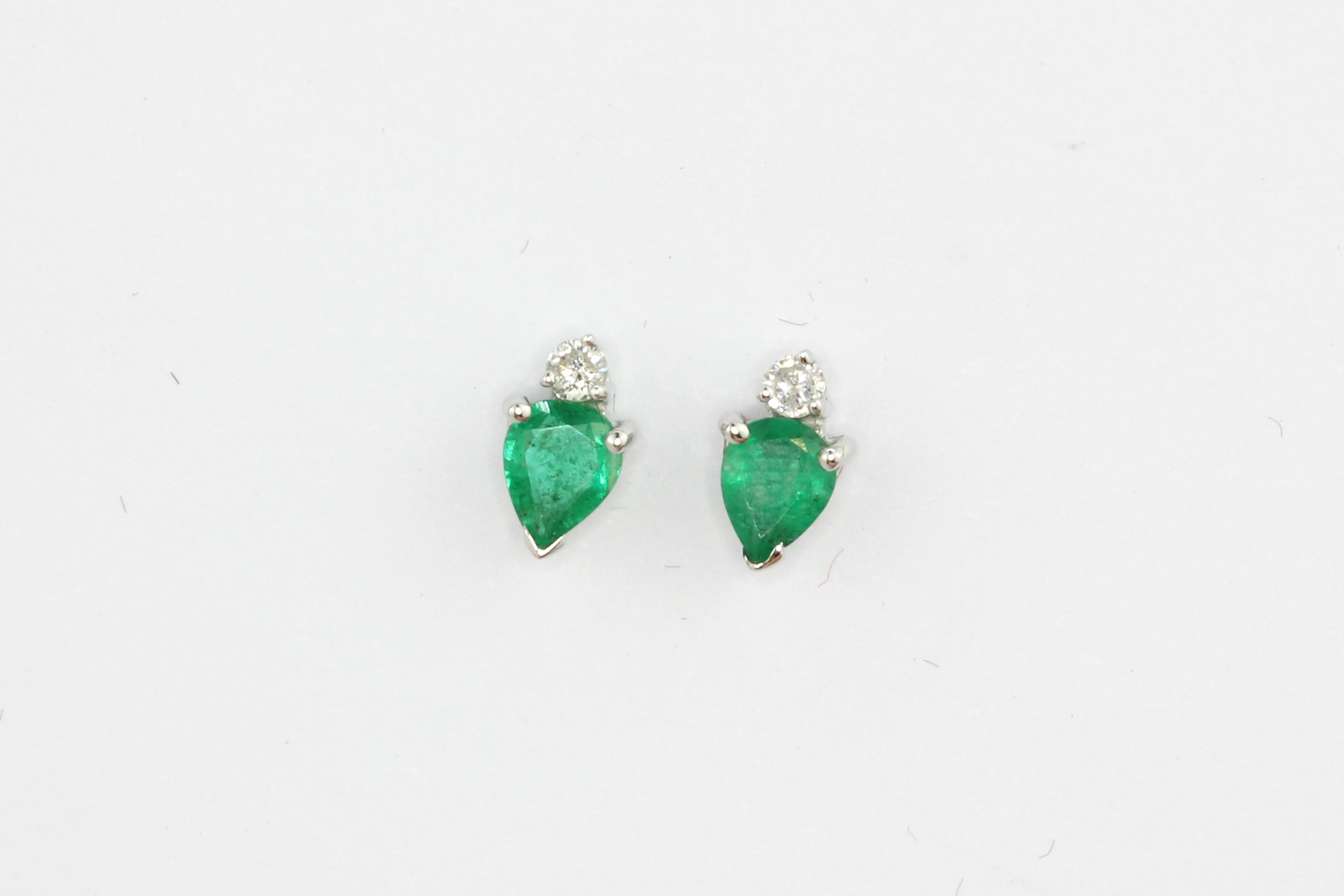 A pair of 14ct white gold stud earrings set with pear cut emeralds and brilliant cut diamonds, L.