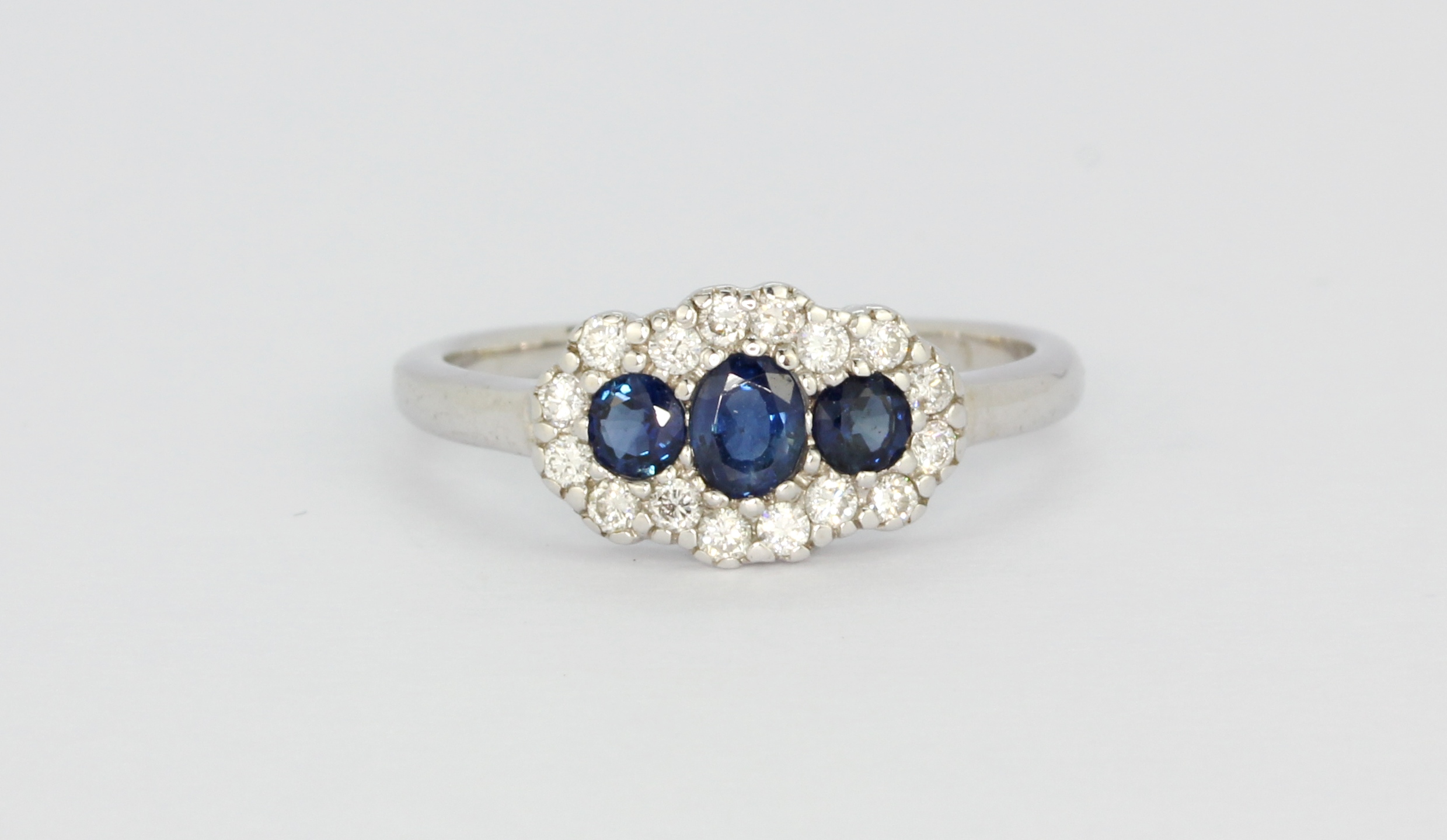 An 18ct white gold triple cluster ring set with oval cut sapphires and diamonds, (L).