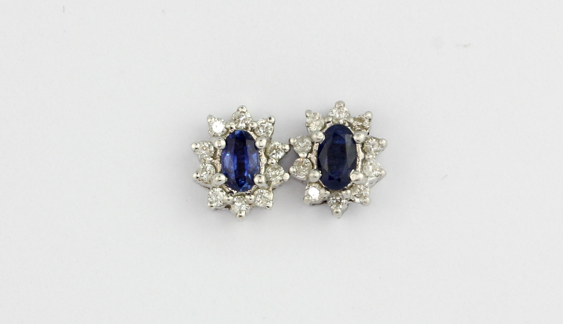 A pair of 18ct white gold (stamped 750) cluster earrings set with oval cut sapphires surrounded by