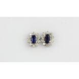 A pair of 18ct white gold (stamped 750) cluster earrings set with oval cut sapphires surrounded by