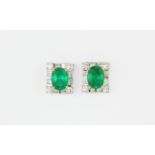 A pair of 18ct white gold (stamped 750) earrings set with oval cut emeralds surrounded by