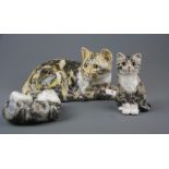 Three handmade Winstanley pottery cat figures with glass eyes, largest H. 16cm W. 31cm.