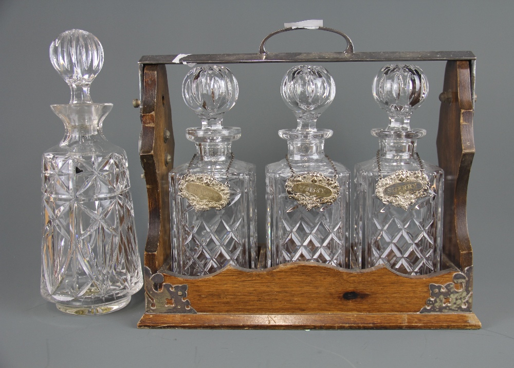 A wood and silver plated tantalus with three cut glass decanters and hallmarked silver spirit labels