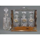 A wood and silver plated tantalus with three cut glass decanters and hallmarked silver spirit labels