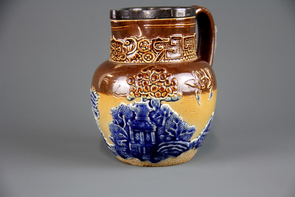 A hallmarked silver rimmed Doulton Lambeth jug decorated with willow pattern, assayed London c.