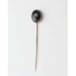 A yellow metal (tested minimum 9ct gold) stick pin set with a cabochon cut agate and a split