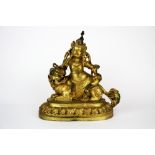 A Tibetan gilt bronze figure of a Buddhist deity seated on a snow lion (remnants of red pigment to
