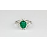 An 18ct white gold (stamped 750) ring set with an oval cut emerald surrounded by brilliant cut