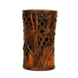 A Chinese carved yellow wood brush pot decorated with stems of bamboo against a lattice