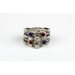 A white metal (tested 18ct gold) ring set with brilliant cut diamonds, rubies and sapphires, (O).
