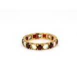 A yellow metal (tested 9ct gold) garnet and white stone set full eternity ring, (K).